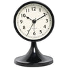 A black round analog alarm clock with a white face and black hands sitting on a pedestal.