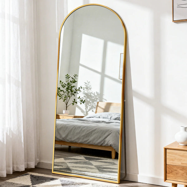 A full length mirror with a gold-toned aluminum frame reflecting a bedroom and a window.