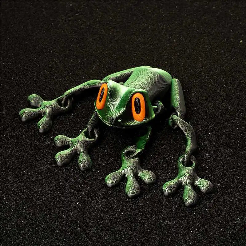 A green magnetic articulated fidget frog with orange eyes resting on a black surface.