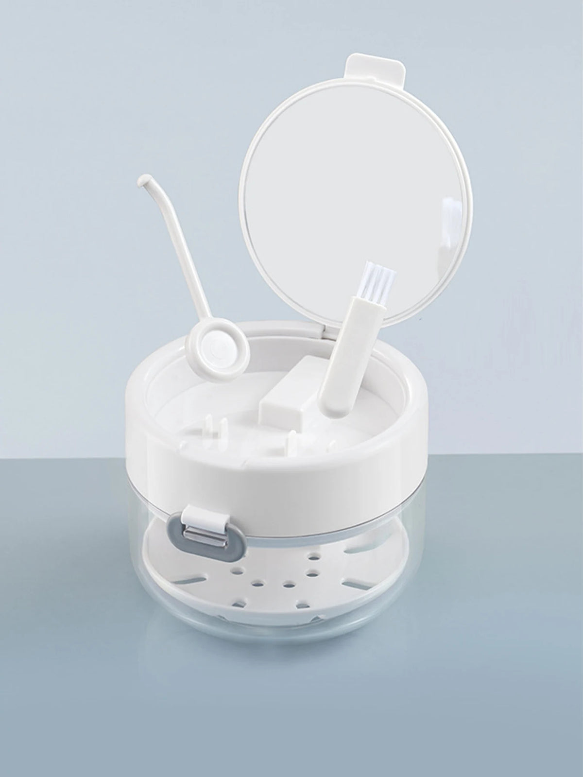 A clear plastic container with a lid and a removable mesh tray holds various dental tools like brushes and instruments.