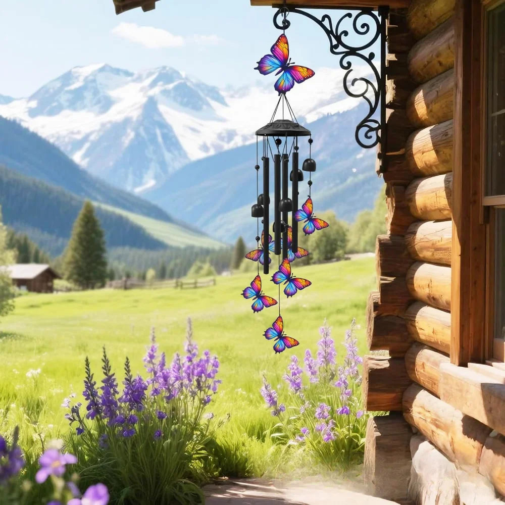 A handcrafted metal wind chime decoration hangs by a window in a rustic wooden cabin with a snowy mountain landscape in the b