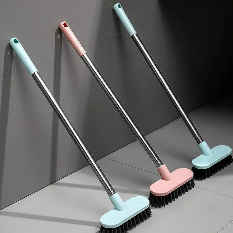 Three long-handle floor scrub brushes in pink and light blue colors are displayed against a gray wall.