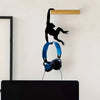 A black silhouette of a monkey hanging from a wooden plank on a white wall above a pair of blue headphones.