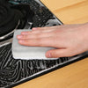A hand is pressing a white cleaning sponge wipe onto a dark, patterned surface.