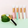 A collection of six silicone facial mask brushes with gold and pastel colored handles displayed on a light surface.
