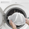 Hands place a white mesh laundry bag over a hat inside a washing machine drum.
