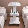 A white portable beauty trolley cart with a top station for tools and a rolling base is shown in a bedroom setting.