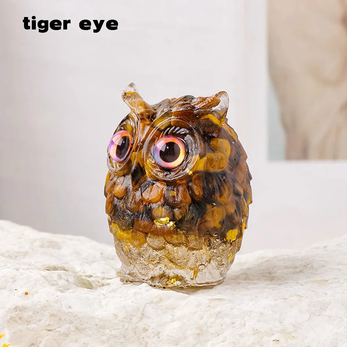 Colgante de búho de piedra natural y triturada con ojos iridiscentes sobre una superficie clara.