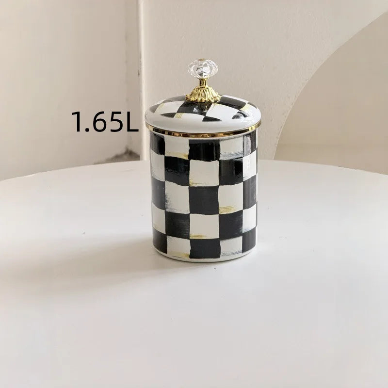 A black and white checkered enamel storage jar with a gold-colored lid sitting on a white surface.