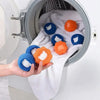 A hand is placing several colorful reusable pet hair and lint remover balls into the drum of a washing machine.