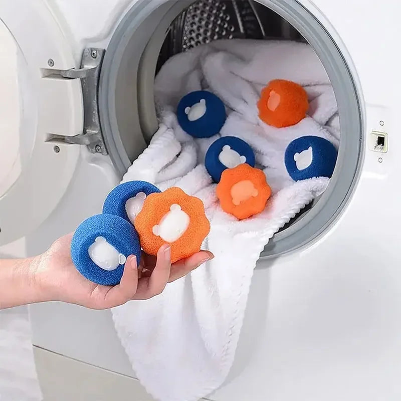 A hand is placing several colorful reusable pet hair and lint remover balls into the drum of a washing machine.
