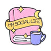 Un pin de esmalte rosa con una pancarta amarilla que dice MY SOCIAL LIFE y una taza morada.