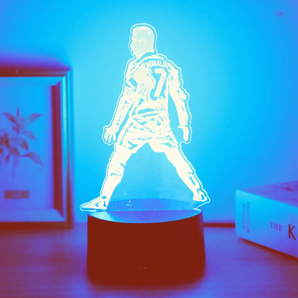A glowing silhouette of a soccer player wearing number 7 stands on a dark base against a bright blue light.
