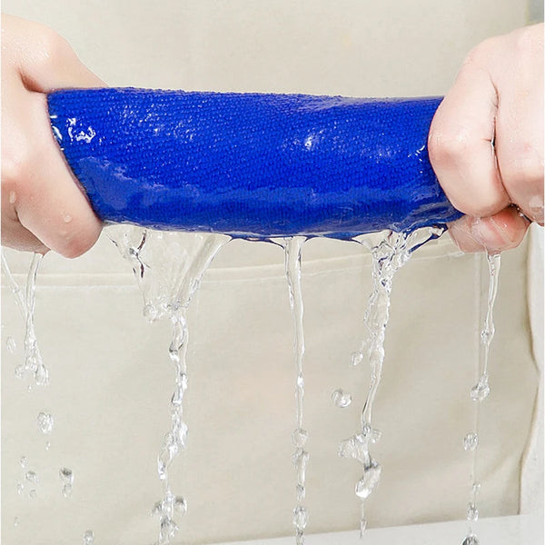 A hand is dripping water from a bright blue thickened microfiber cleaning cloth onto a surface.