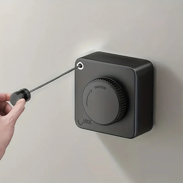 A hand is pulling a black retractable wire clothesline from a wall-mounted fixture.
