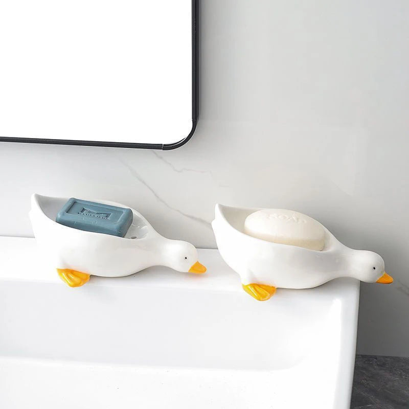 A white ceramic duck shaped soap dish with an orange beak sits on a white bathroom counter.