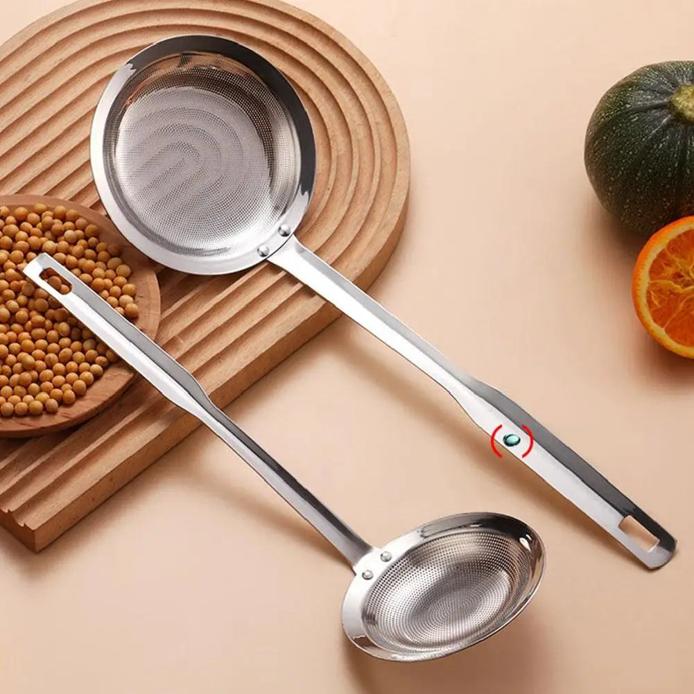 A stainless steel fat skimmer strainer is shown next to a halved green cucumber and a pile of peppercorns on a wooden surface