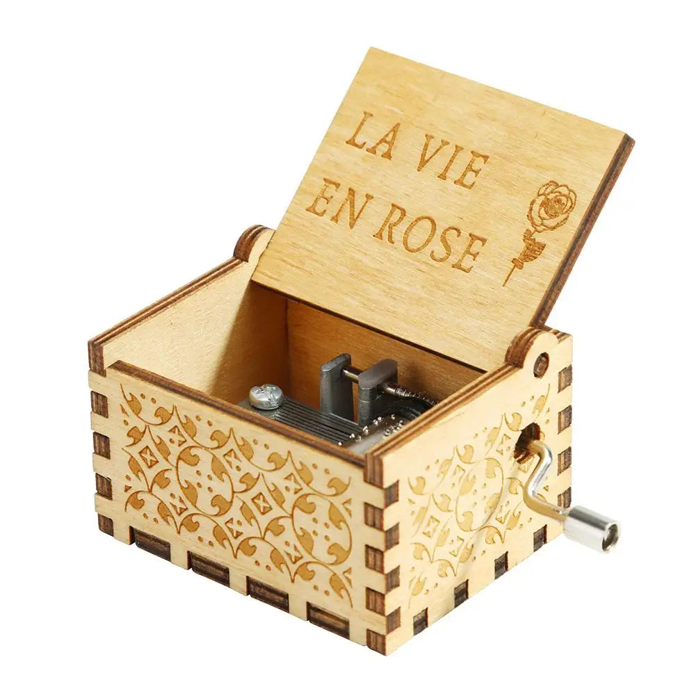 A light wooden music box with a lid engraved LA VIE EN ROSE and a crank mechanism.
