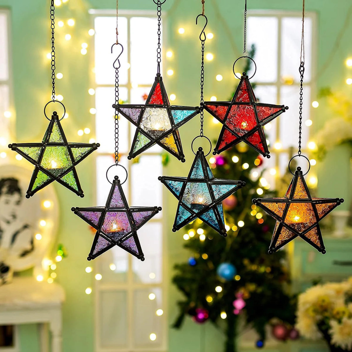 A collection of forged iron star hanging candlesticks with multicolored lights suspended in front of a Christmas tree.