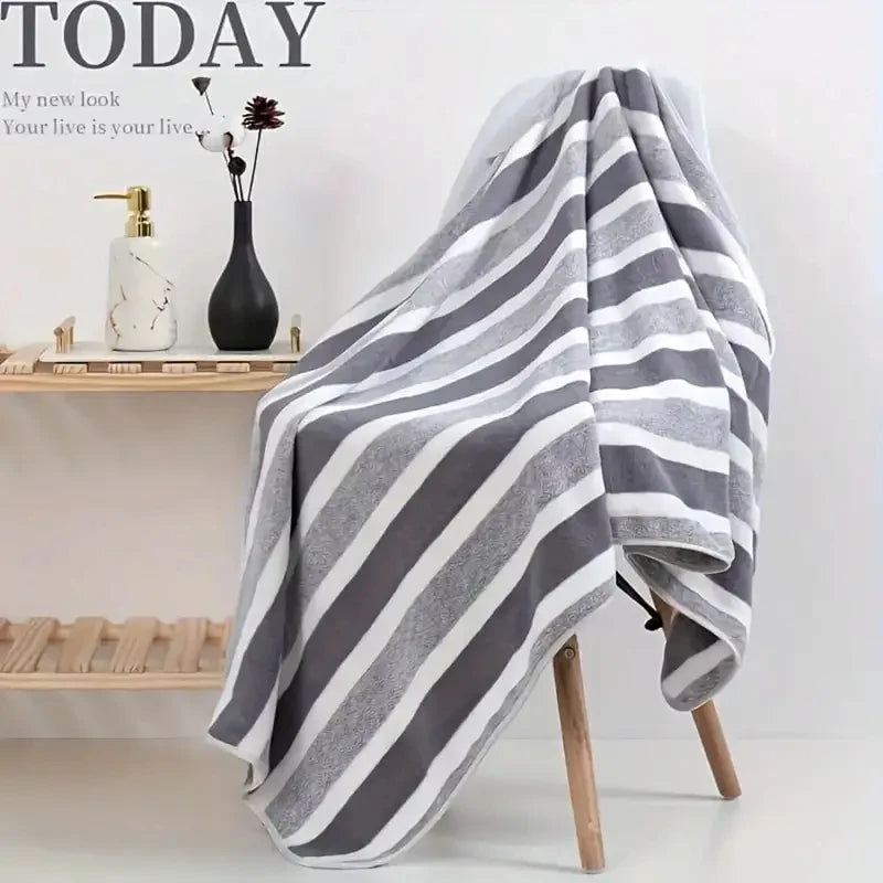 A gray and white striped bath towel draped over a wooden hanger against a white background.