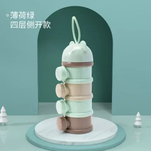 A stack of four light green and pink silicone food storage boxes for baby snacks displayed on a white marble stand.