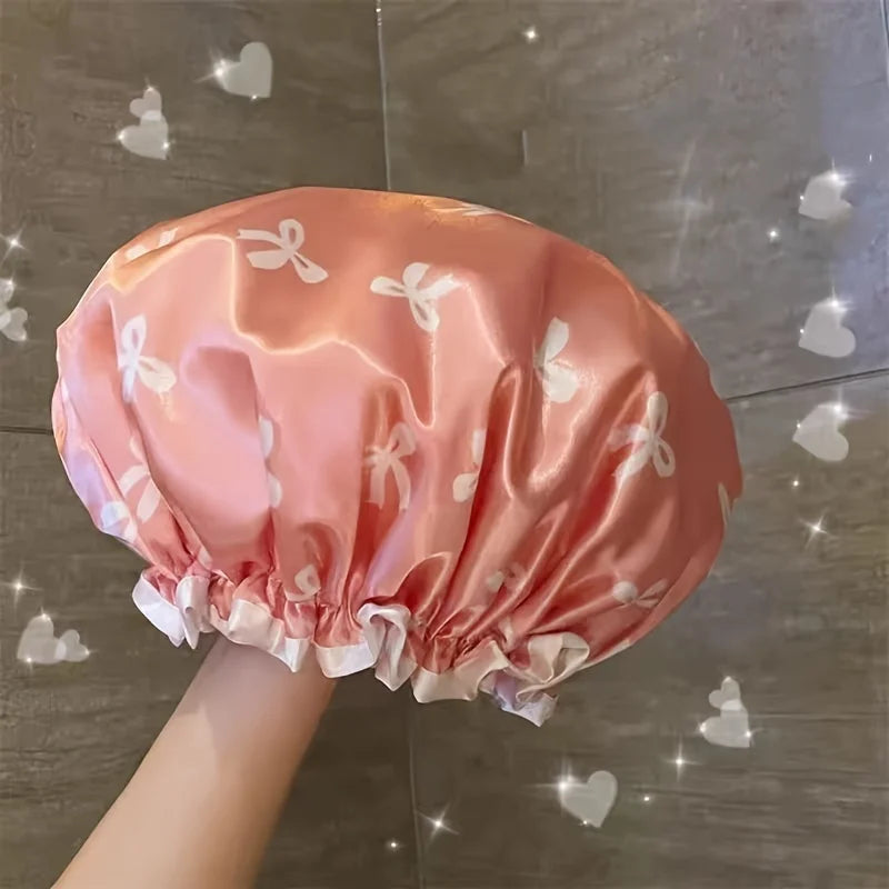 A pink satin reusable double layer shower cap with white butterfly patterns shown from above.