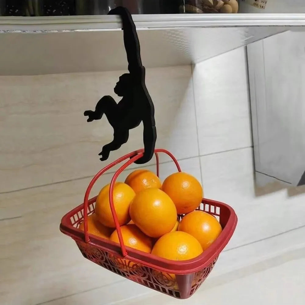A black monkey-shaped wooden key hanger decoration is hanging above a red basket filled with oranges.