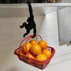 A black monkey-shaped wooden key hanger decoration is hanging above a red basket filled with oranges.