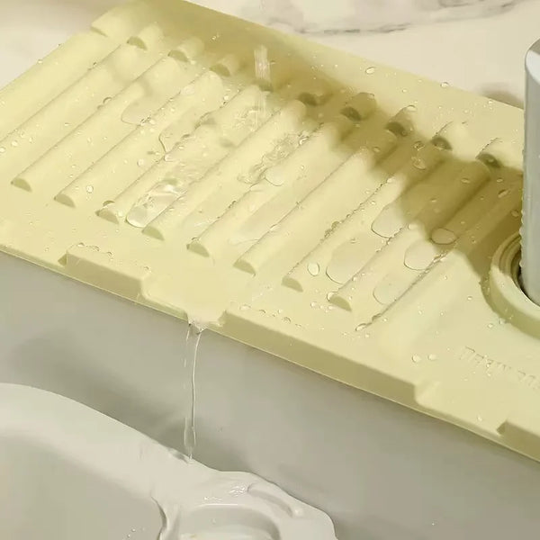 A light yellow splash guard mat is shown dripping water into a sink basin.