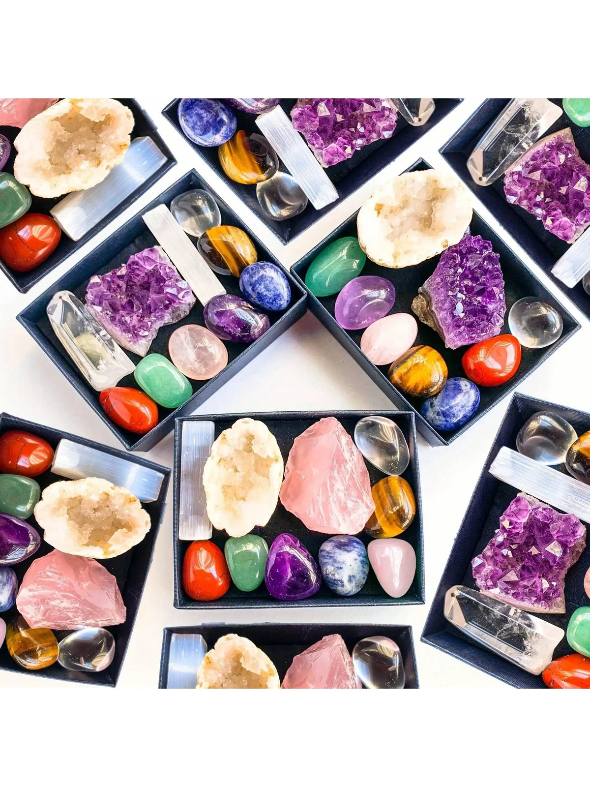 A collection of various natural crystals including amethyst, rose quartz, citrine, and green stones arranged in black trays.