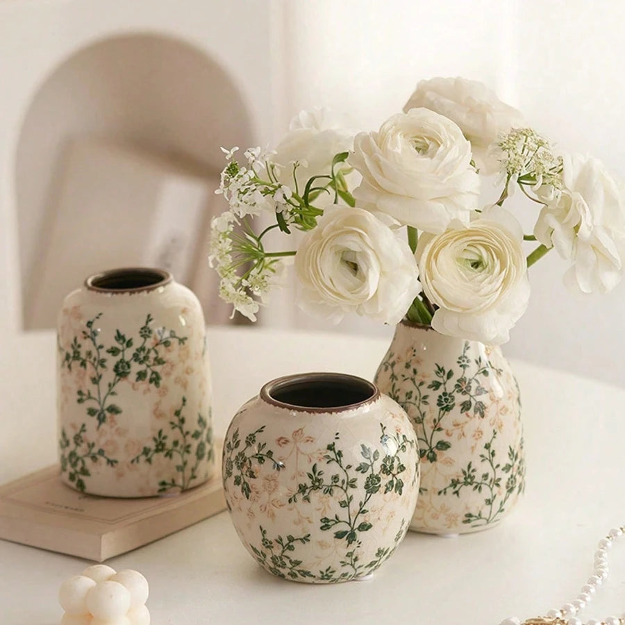 A grouping of white ceramic bud vases with green floral patterns and white roses on a white surface.