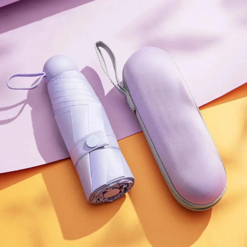 A light purple mini travel umbrella is shown lying on a pink surface with a yellow shadow.