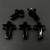 Four black cross pendant charms made of natural agate and jasper displayed on a dark surface.