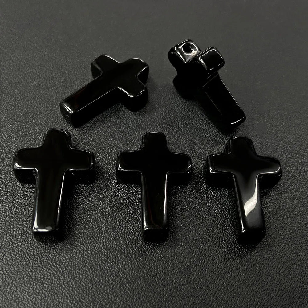 Four black cross pendant charms made of natural agate and jasper displayed on a dark surface.