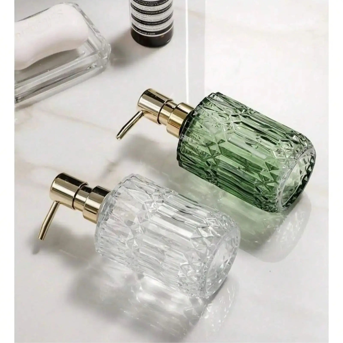 Klares Glas-Seifenspenderflasche mit goldfarbener Pumpe und grüner Flüssigkeit, neben einer weißen Seifen-Nachfüllpackung.