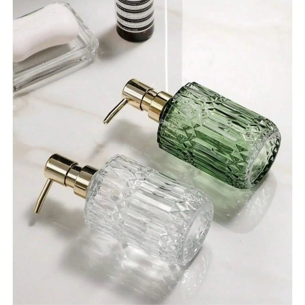 A clear glass soap dispenser bottle with a gold pump mechanism and a green liquid, next to a white soap refill.