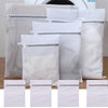 White reusable mesh laundry bags with silver zippers stacked on a wooden surface.