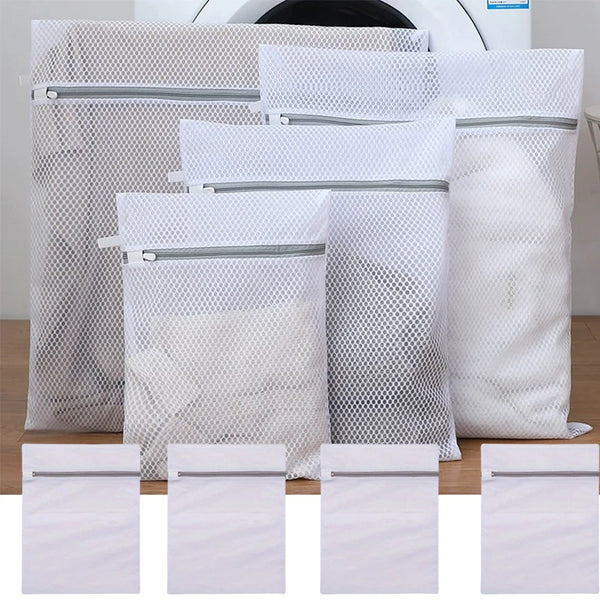 White reusable mesh laundry bags with silver zippers stacked on a wooden surface.