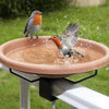 A small bird is splashing water on a copper bird bath disk supported by a stand.
