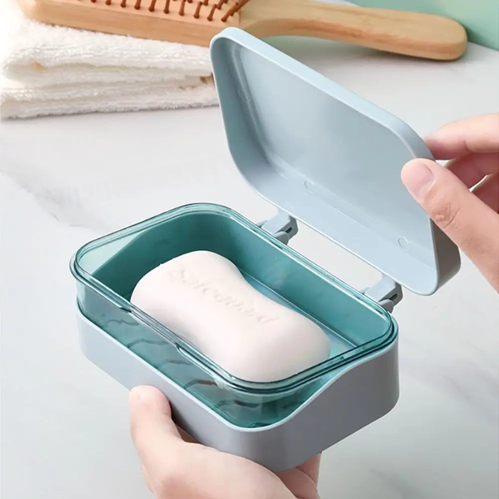 A hand holds an open, light blue transparent drainage soap dish containing a white bar of soap.