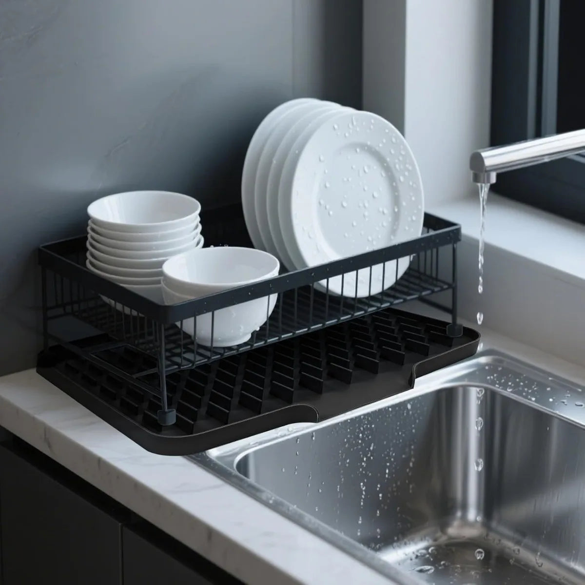 A black silicone drain mat holding white plates and bowls next to a stainless steel kitchen sink.