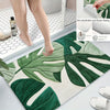 A green and white botanical leaf carpet mat is shown on a floor, with a person's legs standing nearby.