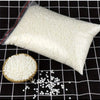 Una bolsa blanca de material para hacer velas de cera de soja junto a gránulos de cera blanca suelta sobre una superficie de 