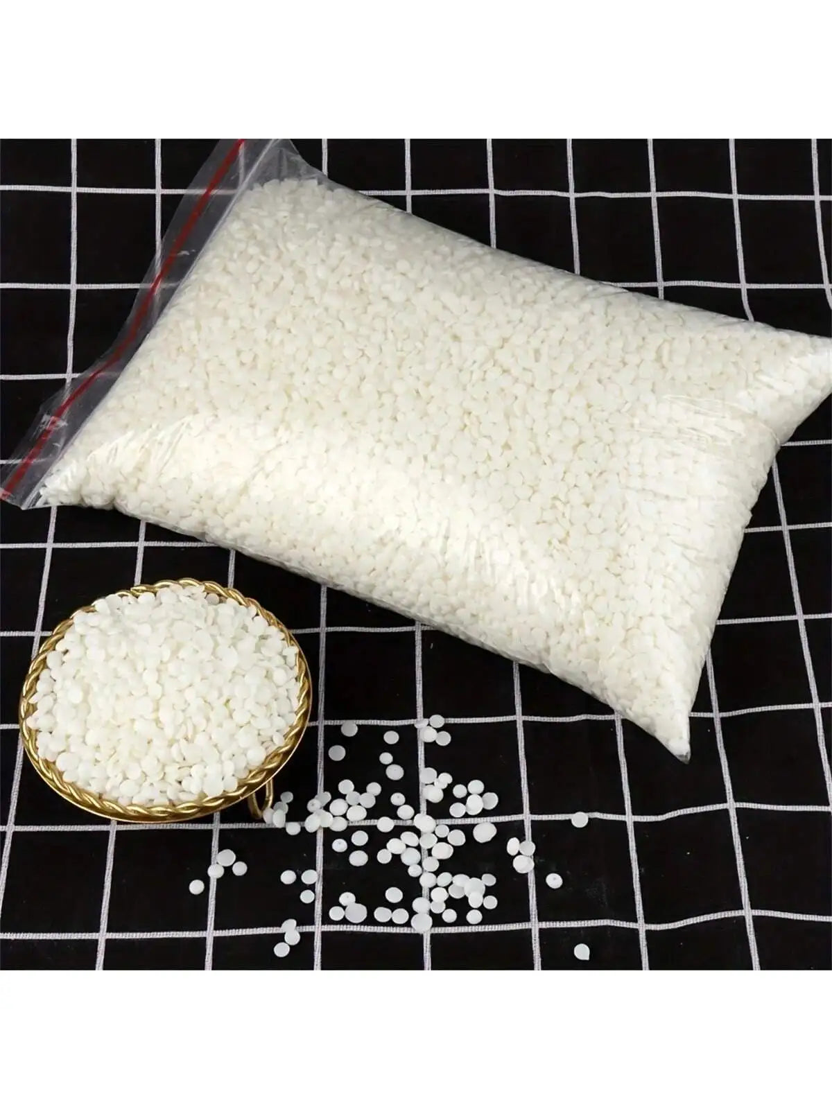 Una bolsa blanca de material para hacer velas de cera de soja junto a gránulos de cera blanca suelta sobre una superficie de 