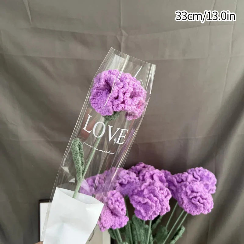 Un vase en verre transparent contient un bouquet de cœurs de coton violet, faits main, avec le mot 'LOVE' écrit sur le verre.