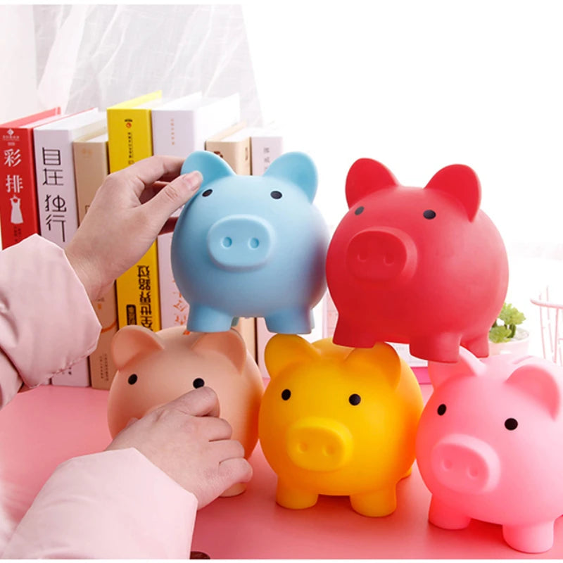 A collection of colorful vinyl piggy banks in blue, red, and yellow are shown being held by a hand on a pink surface.