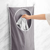 A hand is placing a folded gray towel into the circular pocket of a gray fabric laundry basket organizer hanging on a wall.