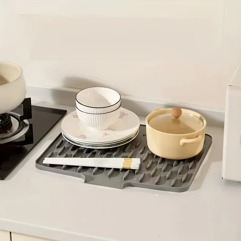 A silicone dish drying mat with raised drainage ridges, holding a ceramic bowl and plates.