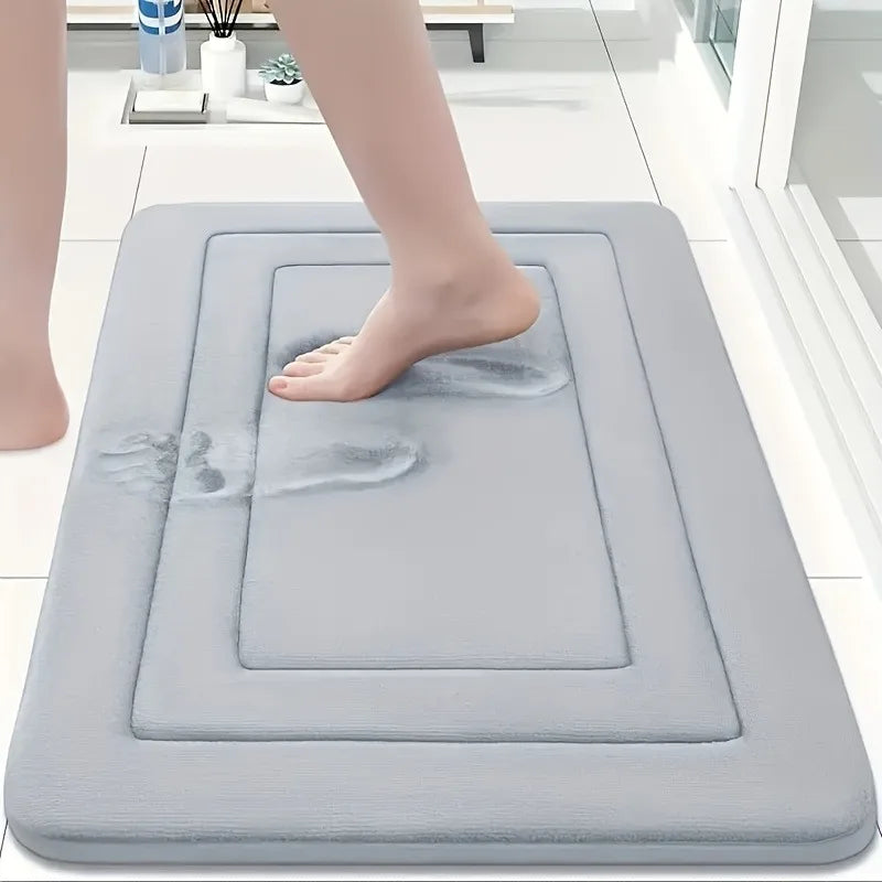 A person's foot is placed on a gray non-slip absorbent bath mat for floors.