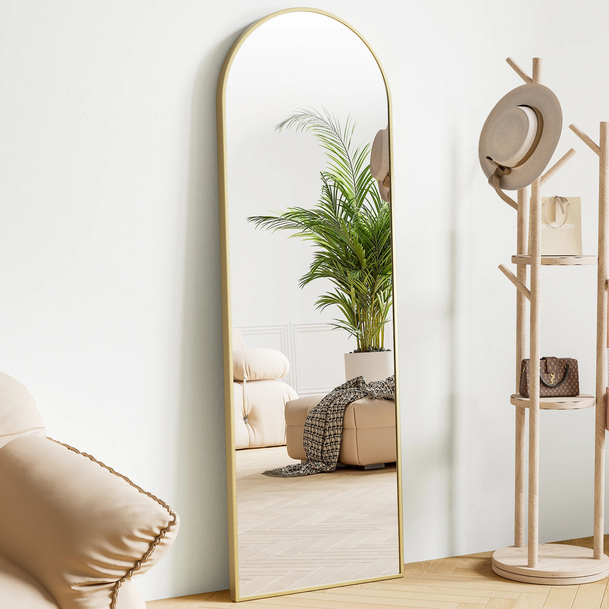 A full body standing wall mirror with a gold frame reflects a potted palm plant and a light-colored sofa.